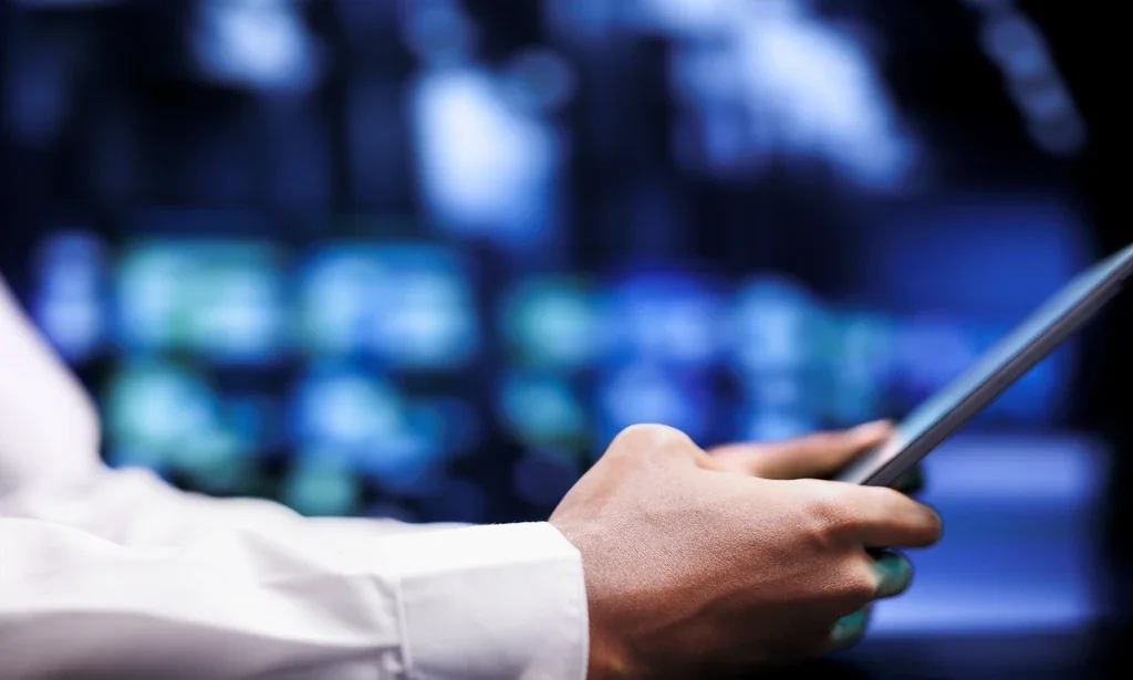 Una persona consulta una tableta frente a pantallas de monitoreo