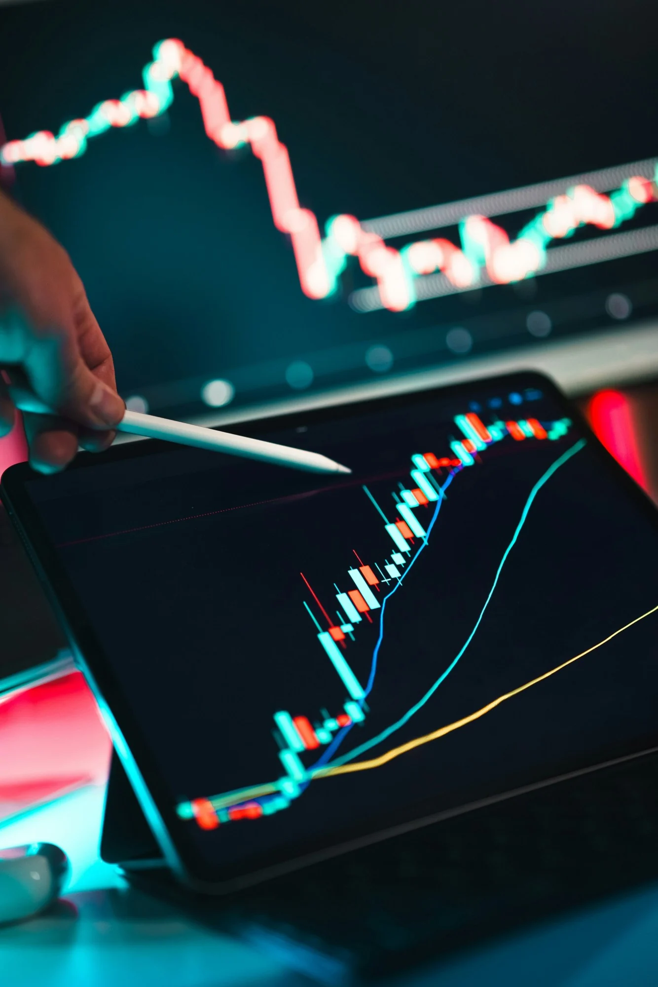 An analyst points a stylus at a candlestick chart on a tablet, with a market data screen in the background